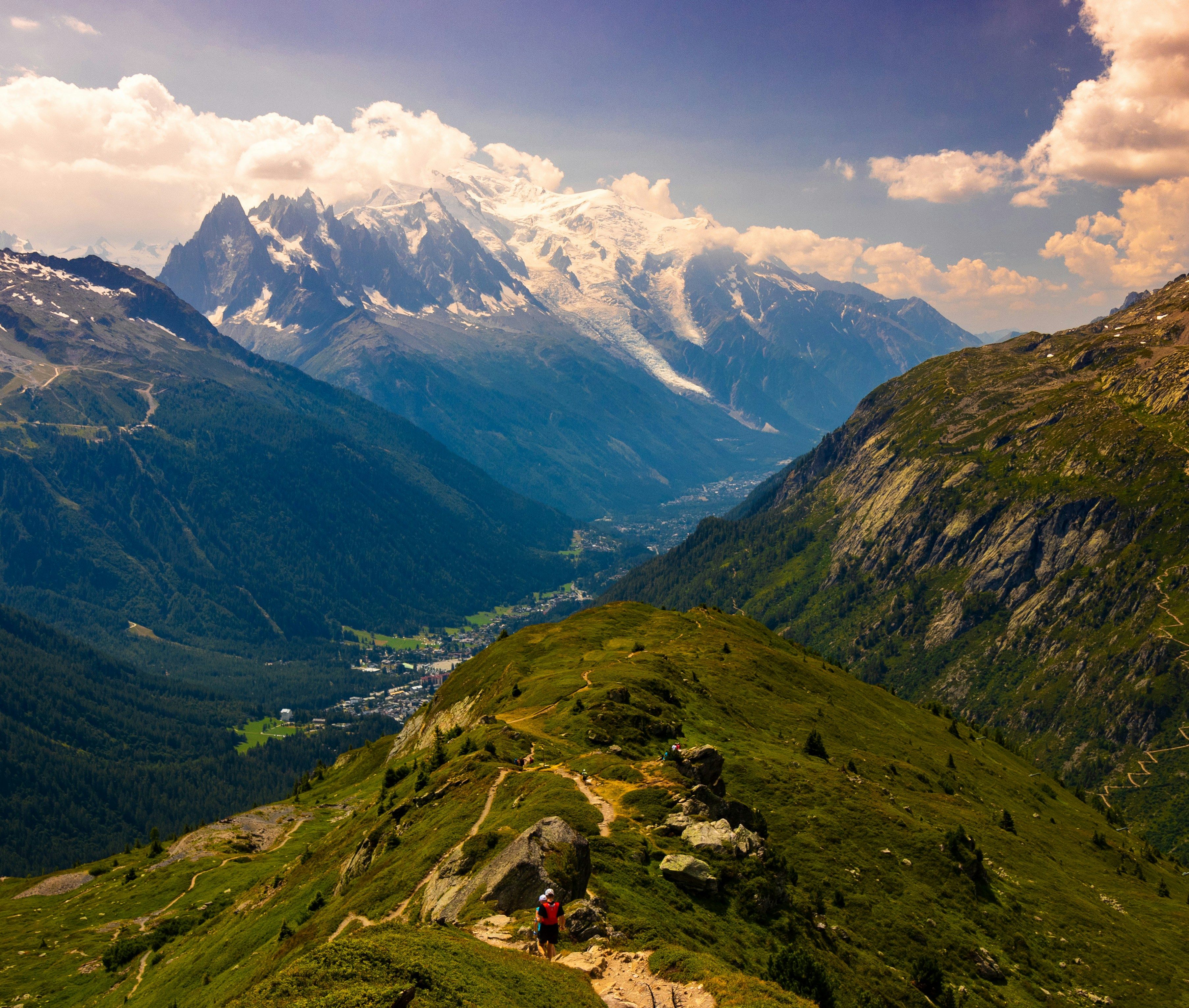 Small figures on a mountain slope with snow-covered peaks in the distance.